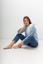 young caucasian pretty girl with long hair in shirt, blue jeans sits at studio Royalty Free Stock Photo