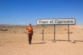 Young caucasian red-haired girl traveler backpacker on the background of a road sign Tropic of Capricorn in the Namib desert, Nami Royalty Free Stock Photo