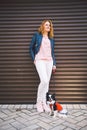 A young Caucasian red-haired woman stands near a city embossed wall with her pet dog, a Chihuahua breed. Walk with a funny dog in Royalty Free Stock Photo