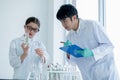 Young Caucasian scientist child girl hold flask with plant tissue and explain to her Asian teacher with record some data during do Royalty Free Stock Photo