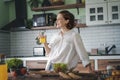 Young caucasian smiling woman drinking orange juice while standing in the kitchen at home Royalty Free Stock Photo