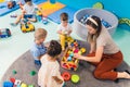 young Caucasian teacher sitting with her kids and playing with plastic toys, kindergarten and creative games concept Royalty Free Stock Photo