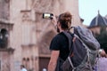 young caucasian traveler man with beard backpack on his back making a photo with the smartphone of him to the facade of Royalty Free Stock Photo