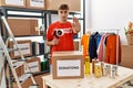Young caucasian volunteer man packing donations box at charity center with open hand doing stop sign with serious and confident Royalty Free Stock Photo