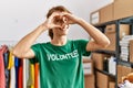 Young caucasian volunteer woman smiling happy doing heart symbol with hands over eye at charity center