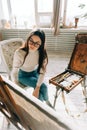 Young caucasian woman artist holding paintbrush and draws on canvas working on a home studio Royalty Free Stock Photo