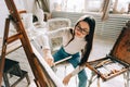 Young caucasian woman artist holding paintbrush and draws on canvas working on a home studio Royalty Free Stock Photo