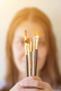 Young caucasian woman artist painter in white shirt holds in stretched hands bunch of different types of paint brushes. Arts