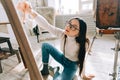 Young caucasian woman artist sitting on a floor holding paintbrush and draws on canvas working on a home studio Royalty Free Stock Photo