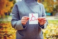 Young Caucasian woman in autumn park showing piece of paper with transgender symbol drawn in it. Human rights day concept.