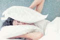 Young caucasian woman with black hair sleeps covering her head and ears with pillows. Royalty Free Stock Photo