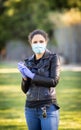 Young Caucasian woman in black leather jacket and surgical mask takes on purple latex gloves