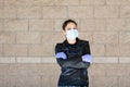 Young Caucasian woman in black leather jacket and surgical mask takes on purple latex gloves Royalty Free Stock Photo