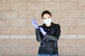 Young Caucasian woman in black leather jacket and surgical mask takes on purple latex gloves