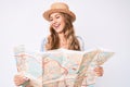 Young caucasian woman with blond hair wearing summer hat holding map smiling and laughing hard out loud because funny crazy joke Royalty Free Stock Photo