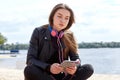 Young caucasian woman in blue red headphones listens to music on the river bank with a digital tablet Royalty Free Stock Photo