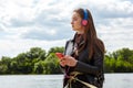 Young caucasian woman in blue red headphones listens to music and typing on the smartphone on the river bank Royalty Free Stock Photo