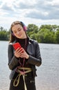 Young caucasian woman in blue red headphones listens to music and typing on the smartphone on the river bank Royalty Free Stock Photo