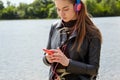 Young caucasian woman in blue red headphones listens to music and typing on the smartphone on the river bank Royalty Free Stock Photo