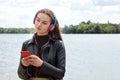 Young caucasian woman in blue red headphones listens to music and typing on the smartphone on the river bank Royalty Free Stock Photo