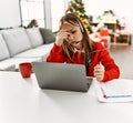 Young caucasian woman call center agent stressed teleworking sitting by christmas tree at home Royalty Free Stock Photo