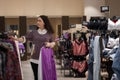 Young Caucasian woman chooses clothes in store. In background there are fitting rooms and hangers with clothes. Concept Royalty Free Stock Photo