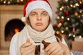 Young Caucasian woman in christmas hat with syrup from coughing, sick due virus or infection, looks at camera with upset