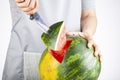 A young caucasian woman is cutting a wedge out of a ripe watermelon using a knife