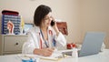 Young caucasian woman doctor talking on phone writing on document at clinic Royalty Free Stock Photo