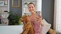 Young caucasian woman with dog smiling taking selfie photo with smartphone sitting on the bed at bedroom Royalty Free Stock Photo