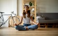 Young caucasian woman doing yoga in lotus pose and eyes closed in an apartment. Relaxation and domestic life