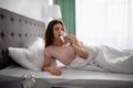 Young Caucasian woman drinking clear mineral water from glass while lying in bed at home Royalty Free Stock Photo