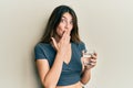 Young caucasian woman drinking glass of water covering mouth with hand, shocked and afraid for mistake