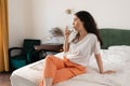 Young Caucasian woman drinks glass of water while sitting on bed. Concept of thirsty and healthy lifestyle Royalty Free Stock Photo