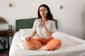 Young Caucasian woman drinks glass of water while sitting crossed legs on bed. Concept of thirsty and healthy lifestyle Royalty Free Stock Photo