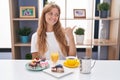 Young caucasian woman eating pastries t for breakfast smiling with happy face looking and pointing to the side with thumb up