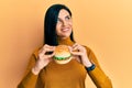 Young caucasian woman eating a tasty classic burger smiling looking to the side and staring away thinking Royalty Free Stock Photo