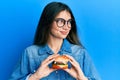 Young caucasian woman eating a tasty classic burger smiling looking to the side and staring away thinking Royalty Free Stock Photo