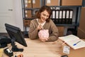 Young caucasian woman ecommerce business worker insert dollar on piggy bank at office Royalty Free Stock Photo