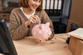 Young caucasian woman ecommerce business worker insert dollar on piggy bank at office Royalty Free Stock Photo