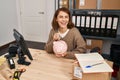 Young caucasian woman ecommerce business worker insert dollar on piggy bank at office Royalty Free Stock Photo