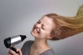 Young caucasian woman girl is blow drying her long hair using electric hair dryer with happy smiling face Royalty Free Stock Photo