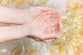 Young Caucasian Woman Girl with Cupped Hands Scoops Up Transparent Sea Water on Rocks and Seaweeds Background. Bright Sunlight Royalty Free Stock Photo