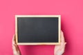 Young Caucasian woman girl holds in hands blank black chalkboard on vibrant fuchsia pink background. Back to school concept