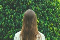 Young Caucasian Woman Girl with Long Chestnut Hair Standing with Back to Viewer on Green Forest Tree Foliage Background