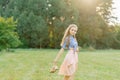 Young Caucasian woman or girl in a summer dress and a denim shirt is walking on the grass, holding shoes in her hands, relaxing Royalty Free Stock Photo