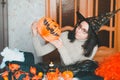 Young caucasian woman with glasses in witch hat prepares for halloween and keeps a pumpkin lantern