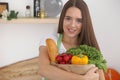 Young caucasian woman in a green apron is holding paper bag full of vegetables and fruits while smiling in kitchen Royalty Free Stock Photo