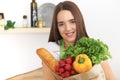 Young caucasian woman in a green apron is holding paper bag full of vegetables and fruits while smiling in kitchen Royalty Free Stock Photo