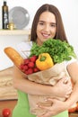 Young caucasian woman in a green apron is holding paper bag full of vegetables and fruits while smiling in kitchen Royalty Free Stock Photo